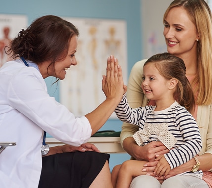 Doctor high-fiving a child being held by her mother.